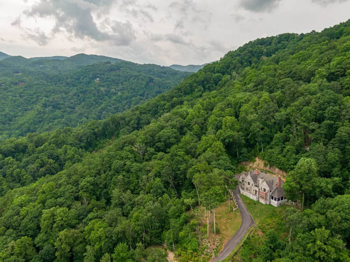 This exterior shot captures the large house surrounded by lush trees and showcases the winding driveway leading up to the property. The landscape hints at the tranquility and seclusion guests will experience, with the house nestled naturally in the mountain environment.