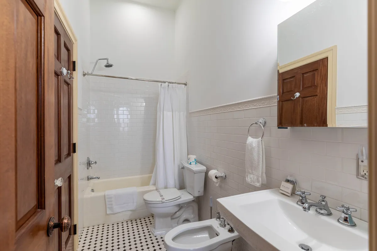 A calm, inviting bathroom featuring a classic bathtub, pedestal sink, toilet, and mirror. The neutral tones and natural light create a spa-like ambiance ideal for relaxation and rejuvenation.