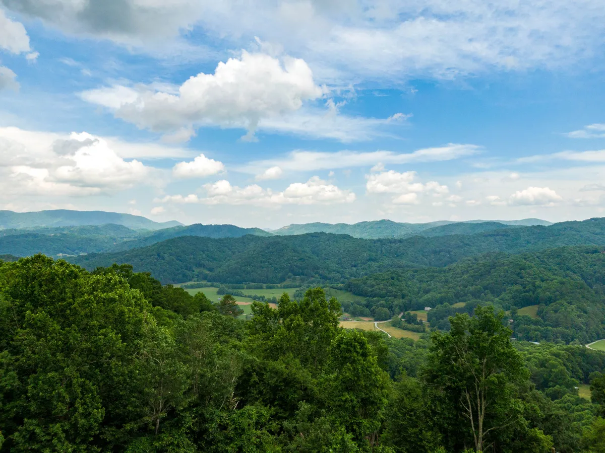 A serene panorama of rolling mountains and lush green forest under a cloudy sky, this view invites thoughts of hiking, photography, or a peaceful family picnic amid nature's grandeur.