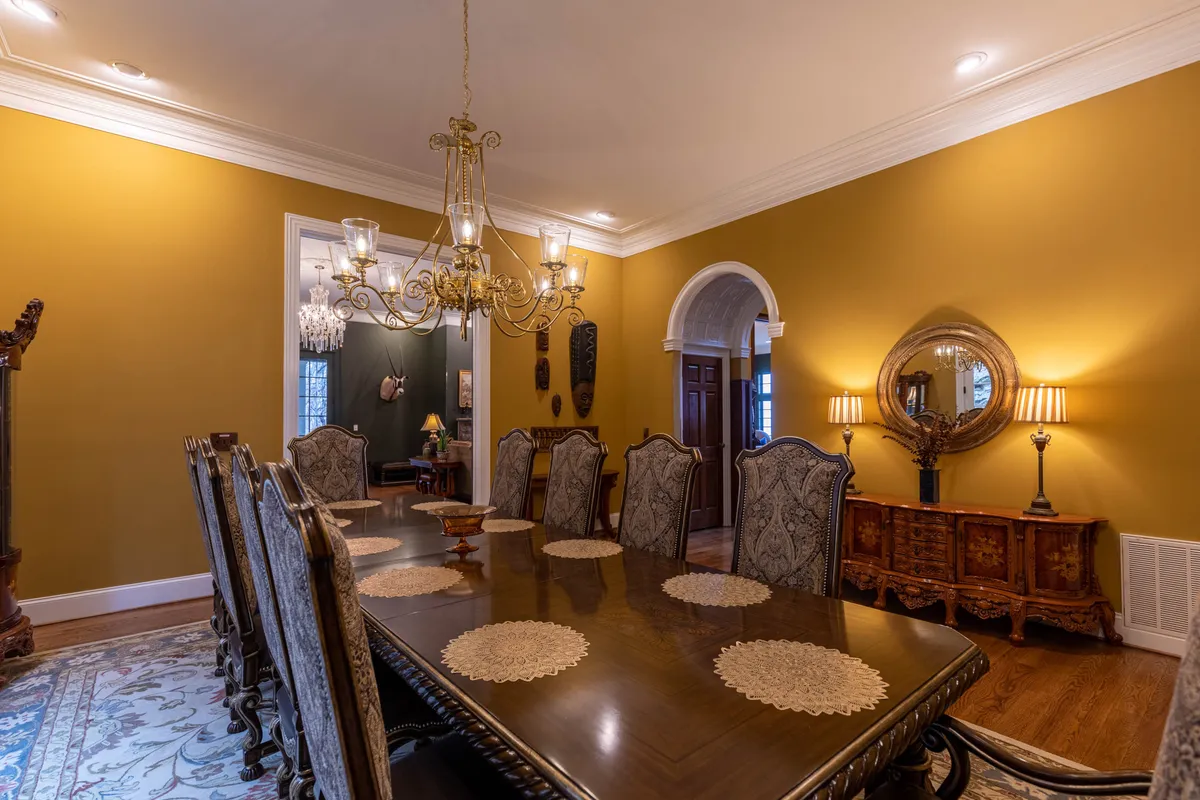 A sophisticated formal dining room is depicted here, with a long dining table, a gleaming chandelier above, elegant décor, and warm lighting. The setting is ideal for hosting grand dinners or family celebrations, exuding an atmosphere of tradition and festivity.