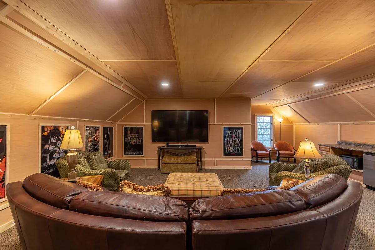 A spacious theater room featuring a large sectional sofa, a television, and artistic movie posters that evoke the ambiance of a private cinema. Soft lighting and comfortable seating invite guests to enjoy movie marathons and group gatherings.