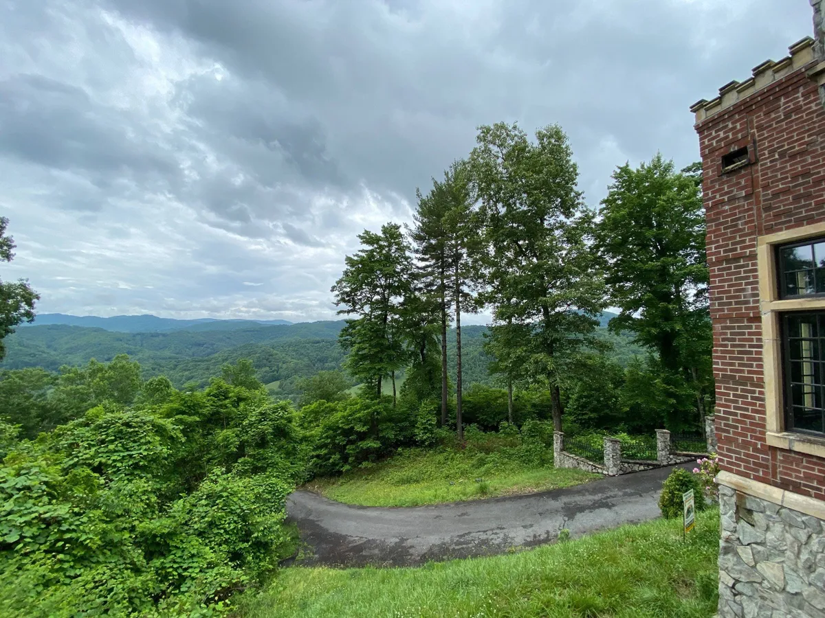 A scenic view featuring a mountain range in the background, lush greenery, and the curved driveway approaching the house’s brick facade. This shot situates the estate within the iconic Appalachian landscape, inviting guests to explore the region’s natural beauty and heritage trails.