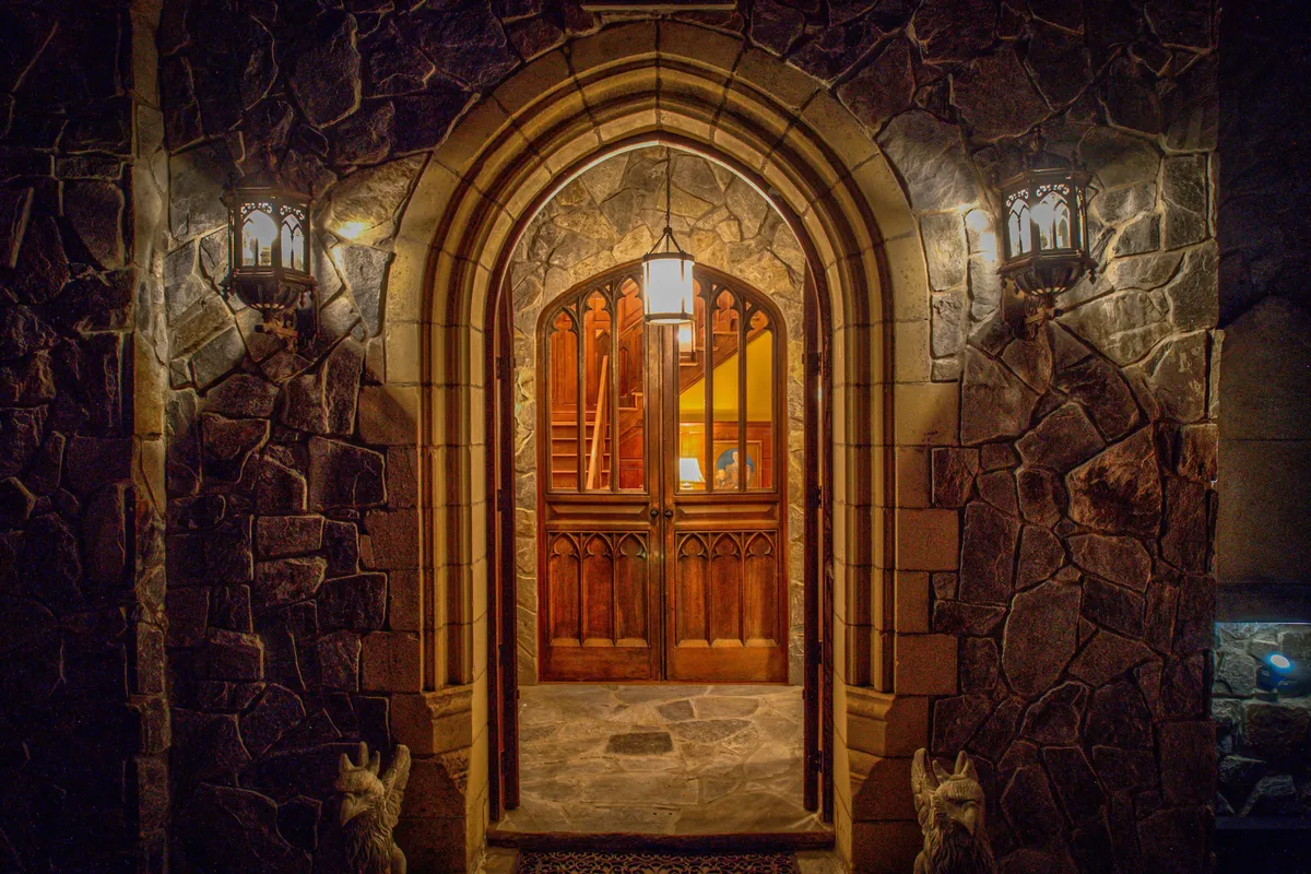 This image captures the mansion's arched stone doorway illuminated by warm lantern light, with texture-rich walls and a glimpse of the inviting interior beyond. The scene evokes a sense of welcome and heritage, hinting at storied gatherings and historic celebrations within.