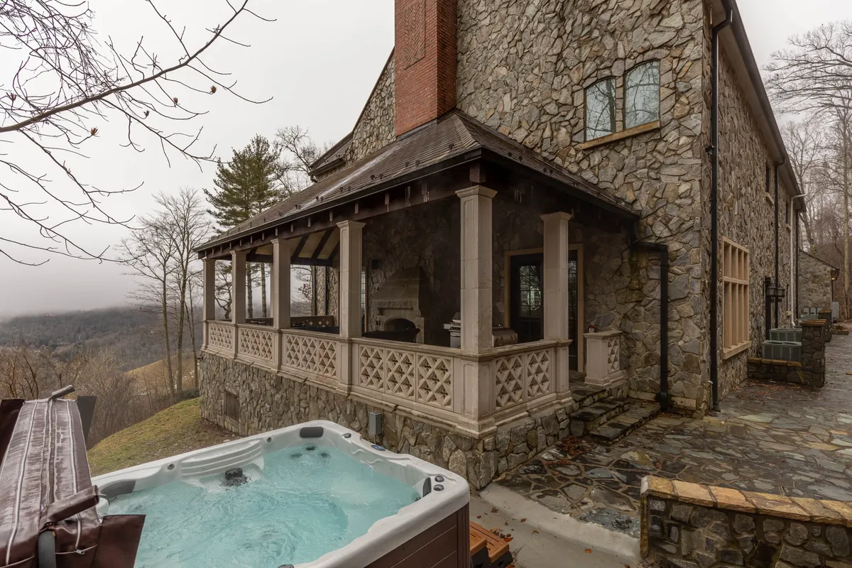 An outdoor area featuring an 8-person hot tub, stone exterior, covered porch space, and panoramic mountain views—inviting relaxation and conviviality in a stunning natural setting.