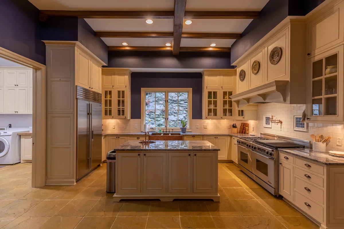 This image showcases a chef's kitchen anchored by a central island with a striking granite countertop, complemented by stainless steel appliances. Large windows brighten the space, connecting it visually to the outdoors and inviting natural light to flow in. The setup is ideal for cooking, entertaining, and family gatherings, with high-end finishes and open sight lines.