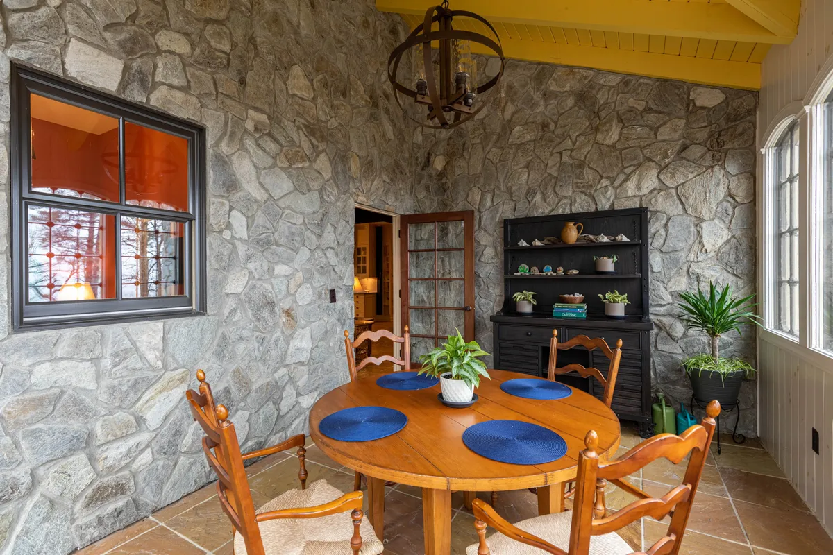 A welcoming breakfast nook with a round wooden table set with blue placemats sits against a stone wall, with green plants and soft lighting lending a cozy, bright atmosphere. The space feels perfect for casual breakfasts or morning coffee, inviting relaxation and everyday connection.