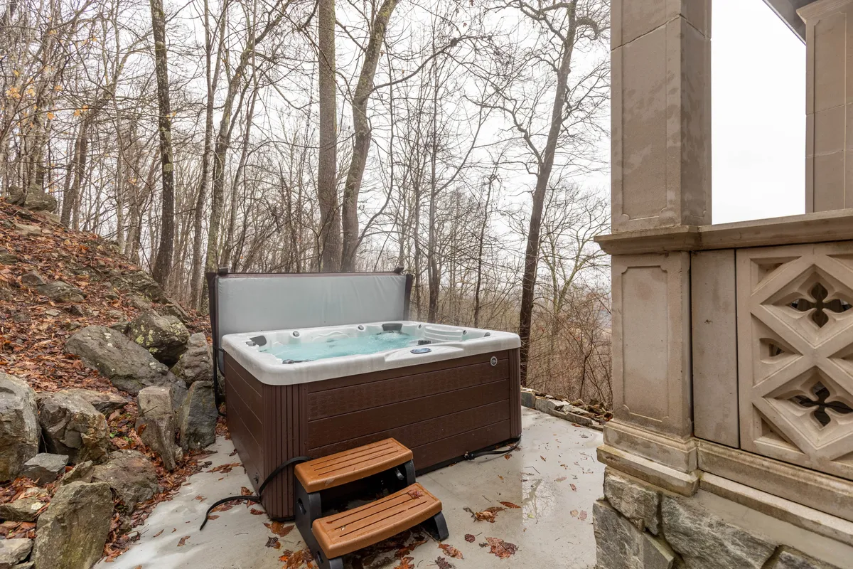A steaming hot tub nestles beside a stone structure, surrounded by tall trees. The serene atmosphere creates an inviting space to relax in nature after a day of exploration, with enough room for friends and family to gather.