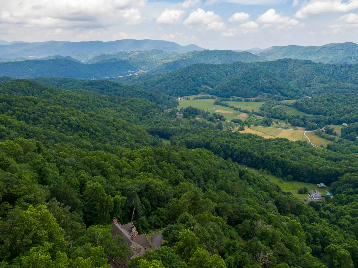 A panoramic view of rolling hills, distant mountains, and verdant forests stretching into the horizon. The landscape is serene, inviting exploration, hikes, and quiet reflection amidst nature.