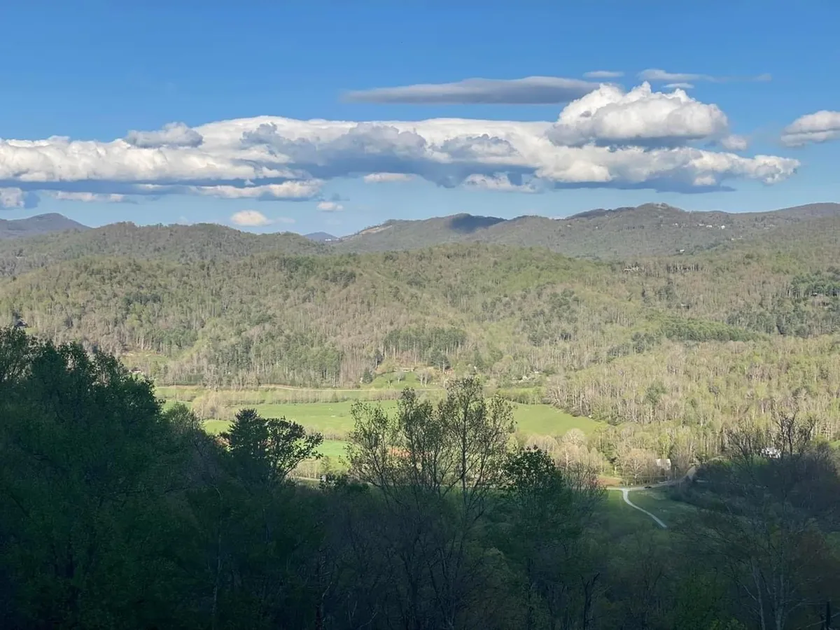A panoramic view of rolling hills, lush greenery, and a cloudy sky. The landscape shifts dramatically with the seasons, offering brilliant fall foliage, wildflower meadows in spring and summer, and serene winter vistas.